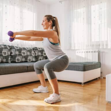 A woman holding dumbbells while doing squats in her living room.