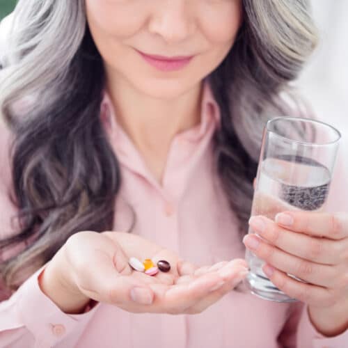 Close up of a middle-aged woman holding dietary supplements and a glass of water.