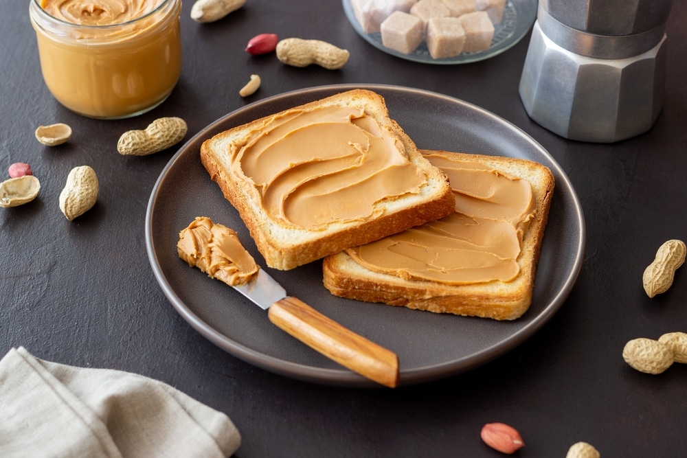 A black plate with two slices of bread topped with peanut butter.