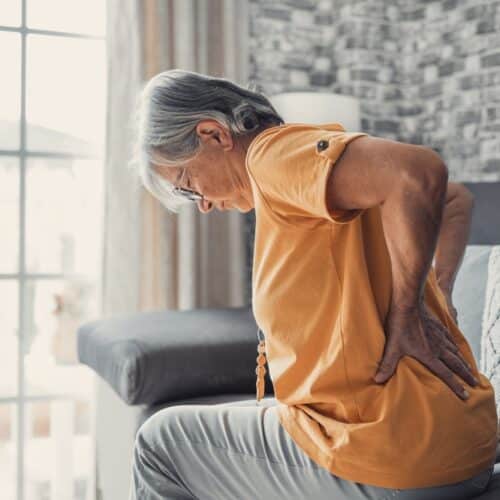 An older woman sitting on the bed with back pain from osteoporosis.