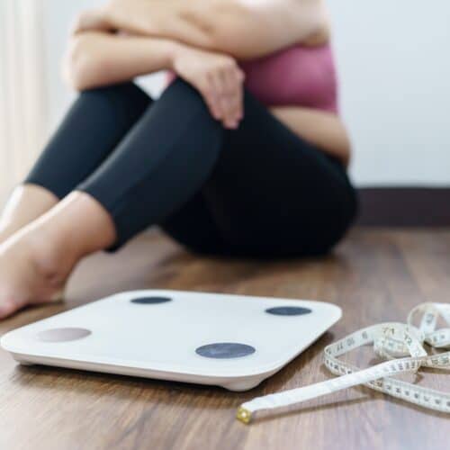 woman sitting on floor next to scale frustrated with weight loss