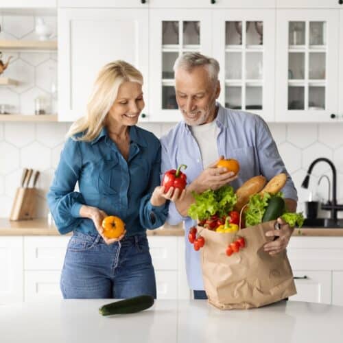 Happy older couple unpacking a bag of groceries in the kitchen.