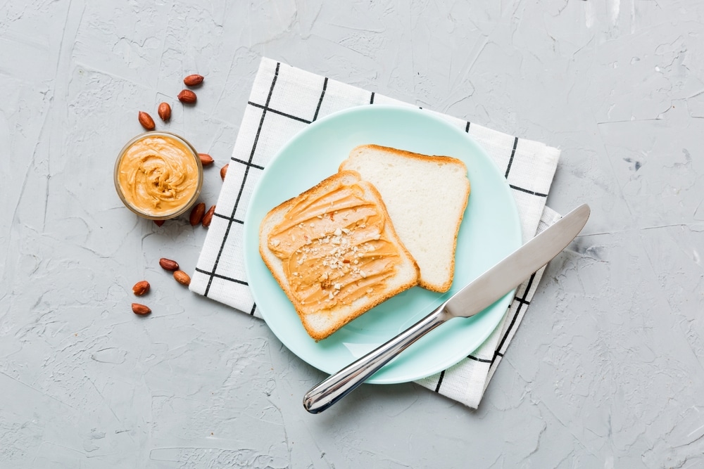 Overhead view of a bread slice topped with peanut butter on a light blue plate.