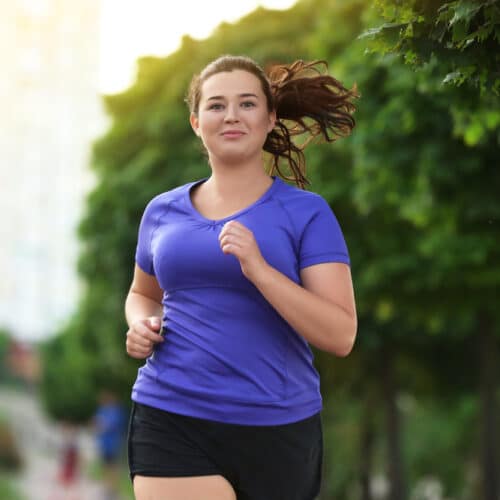 A woman in a purple top jogging outdoors.