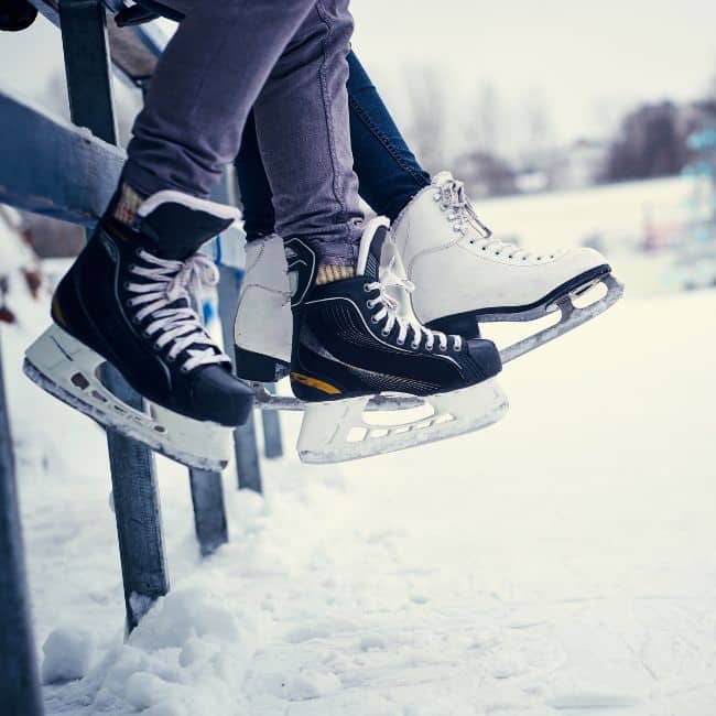 pair of legs with ice skates hanging over bench outside in winter