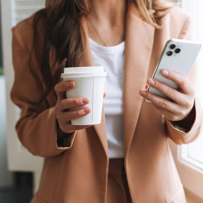 woman in blazer holding coffee and phone