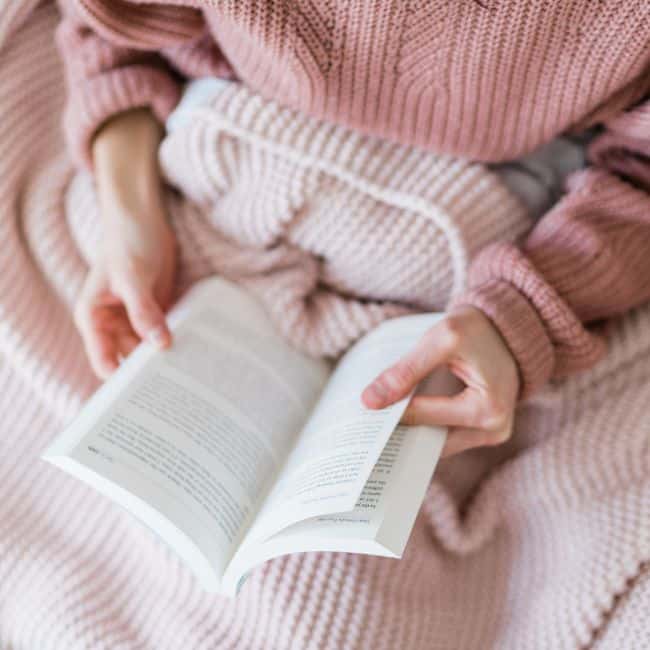 woman in cozy sweater and blanket reading book