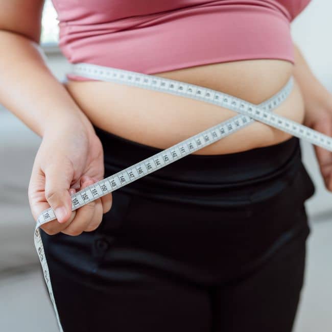 woman holding measuring tape over exposed belly with muffin top