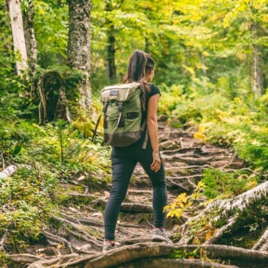 woman doing rucking exercise with weighted backpack on trail