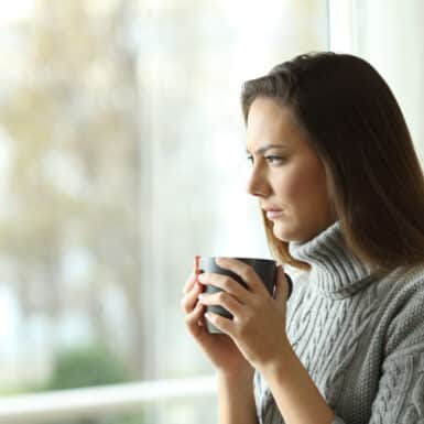 woman sitting holding mug looking sad outside