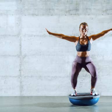 woman doing balance exercise standing with arms out on balance ball half