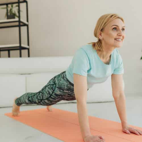 older woman smiling doing plank exercise on yoga mat