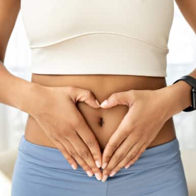 woman holding heart hands over stomach in workout outfit