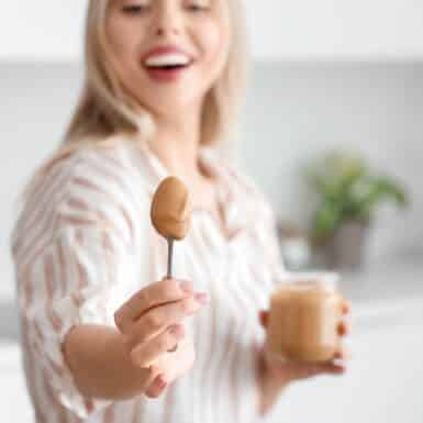 woman smiling with jar and spoon of peanut butter