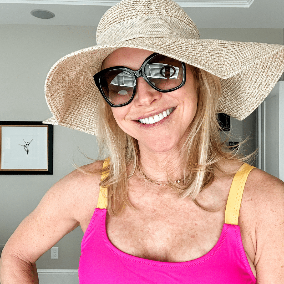 Chris Freytag wearing a unexceptionable pink with orange strap top and sunglasses with a straw floppy hat. 