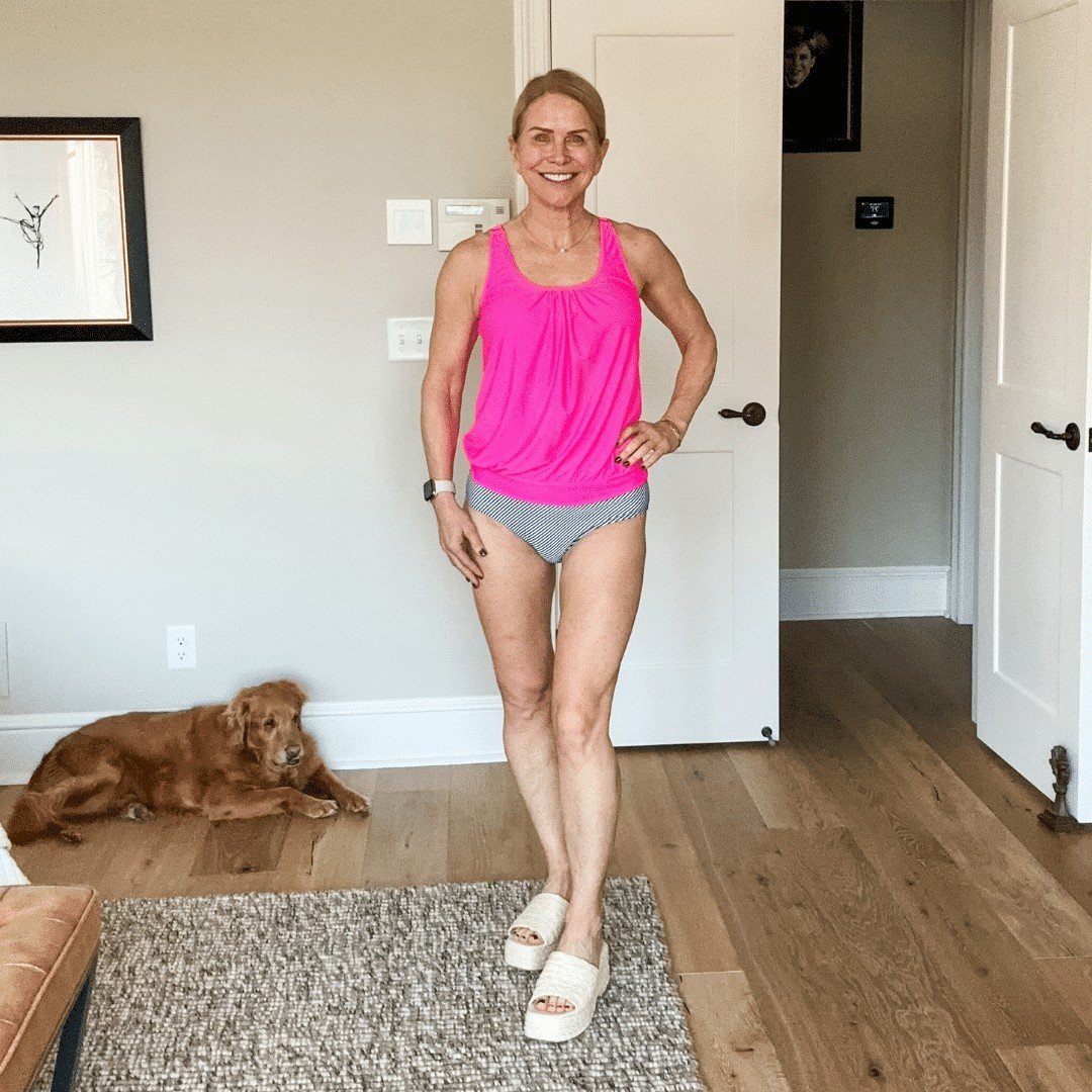 A woman wearing a bright pink tankini swim suit modeling for women over 50 swim suits.