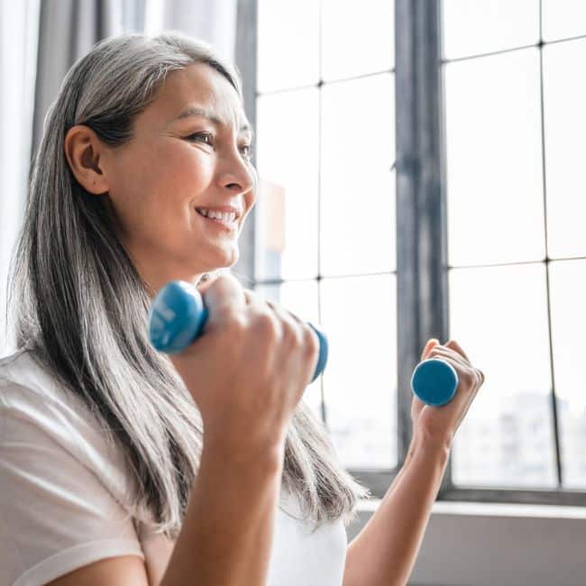 woman doing core exercises for seniors with two small hand weights in natural light from window