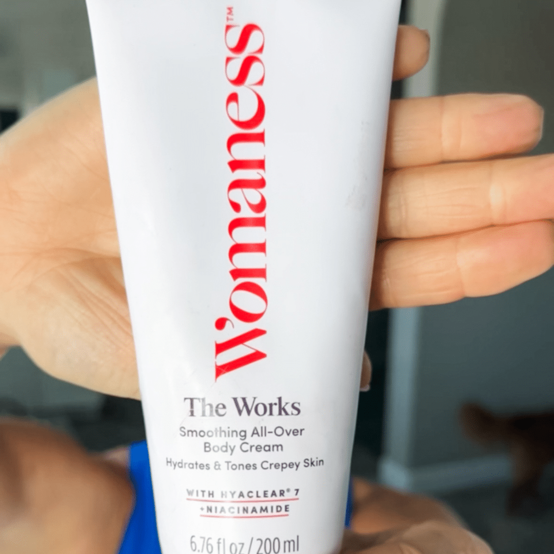 Woman holding up a white bottle of Womaness The Works Body Cream with hand behind it.