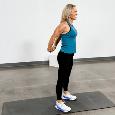 Chris Freytag wearing a blue workout tank and black leggings doing a standing chest expansion.