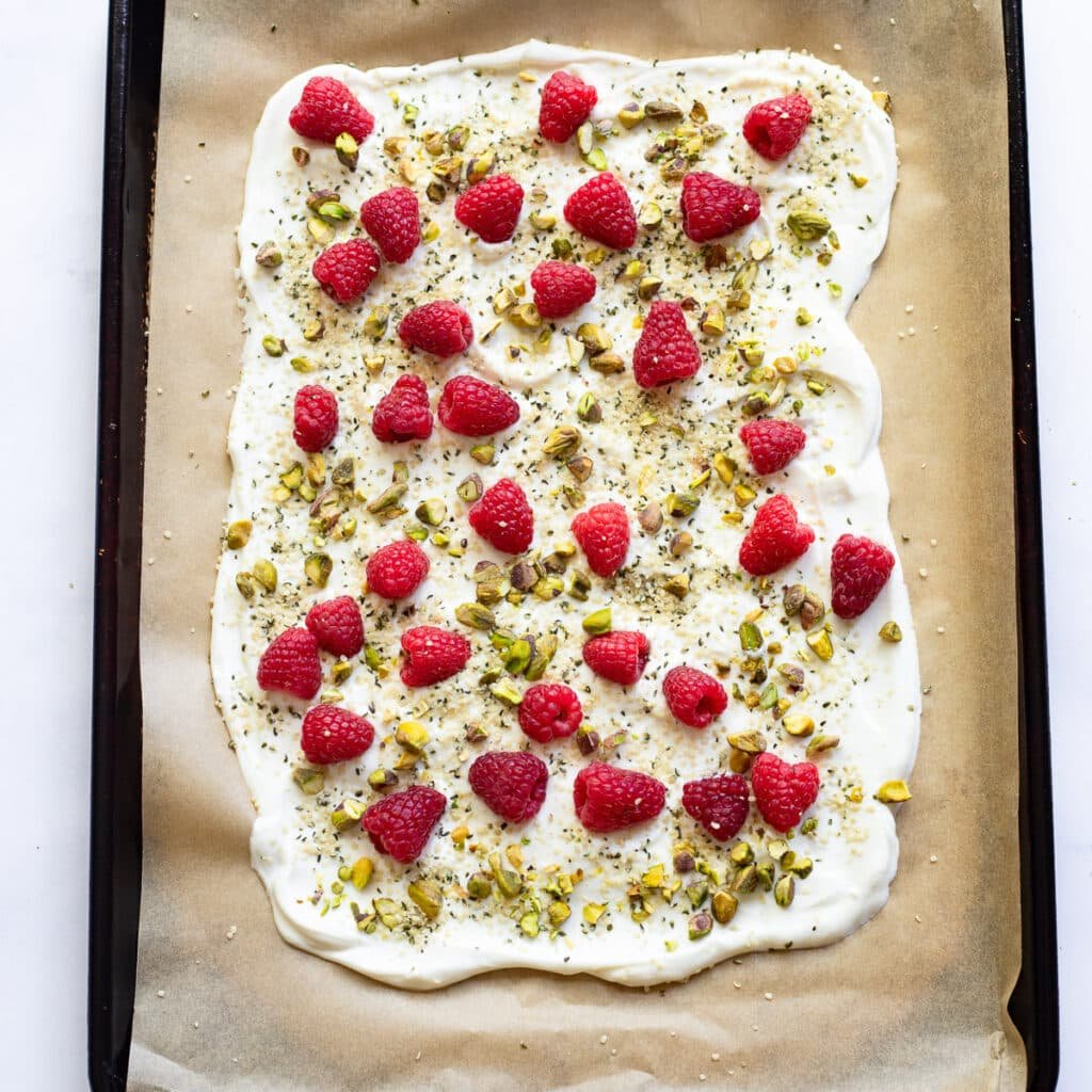 healthy frozen yogurt bark with raspberries and pistachios prepped on parchment paper