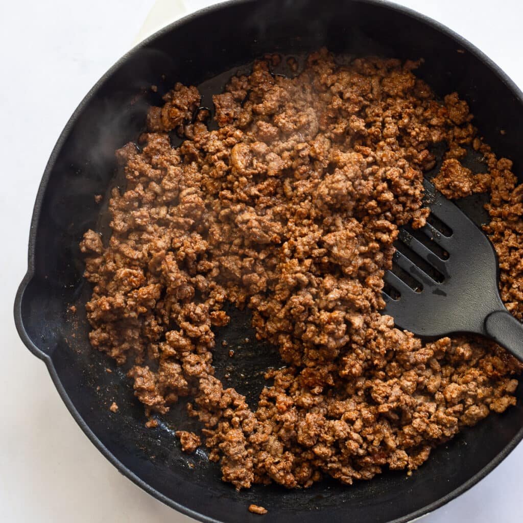 black skillet with ground beef cooking with spatula