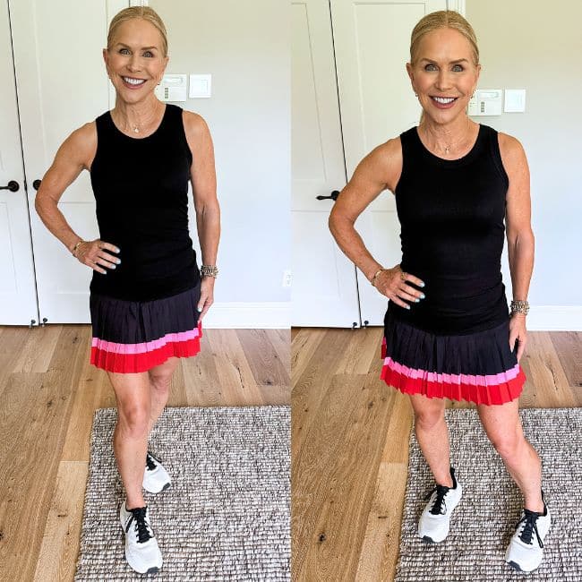 A smiling woman with blonde hair in a ponytail, wearing a black sleeveless top, a black and red skirt, and white sneakers, stands posing with one hand on her hip in a bright room with a rug and white cabinets.