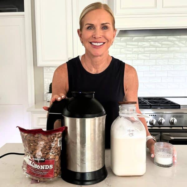 woman smiling in front of almond cow machine and fresh milk in kitchen