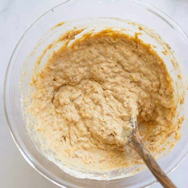 glass bowl with mixed ingredients and wooden spoon for healthy banana bread