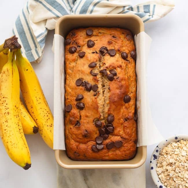 overhead image of prepared healthy banana bread loaf in pan next to bunch of bananas