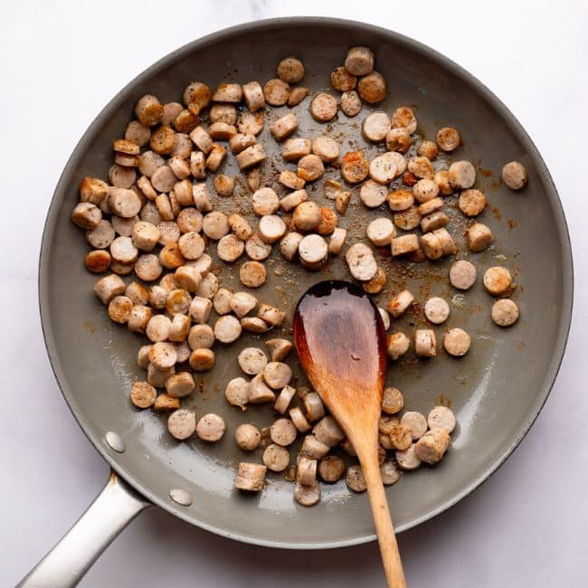 browning sausage in pan with wooden spoon