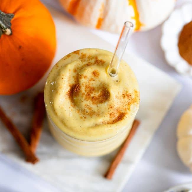 close up top view of healthy pumpkin smoothie served in glass cup with glass straw
