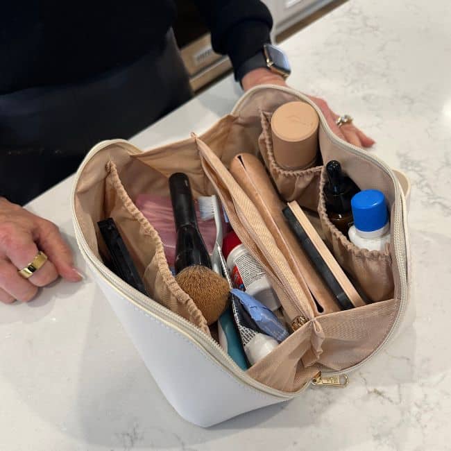 Lay-flat travel makeup bag open on a bathroom counter with toiletries and makeup