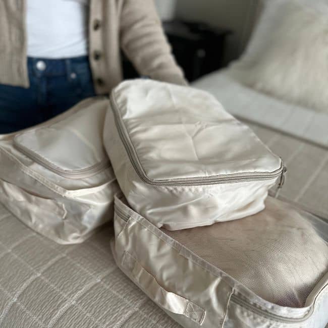Woman over 50 using packing cubes to organize clothes inside a carry-on suitcase