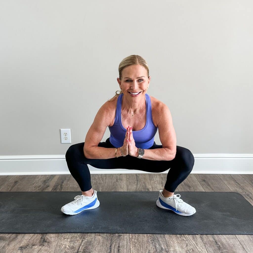 Woman holding a yogi squat with heels down and palms pressed at her chest to open hips and ankles after a walk